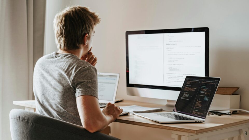 A man sits with multiple computers around him, possibly working.