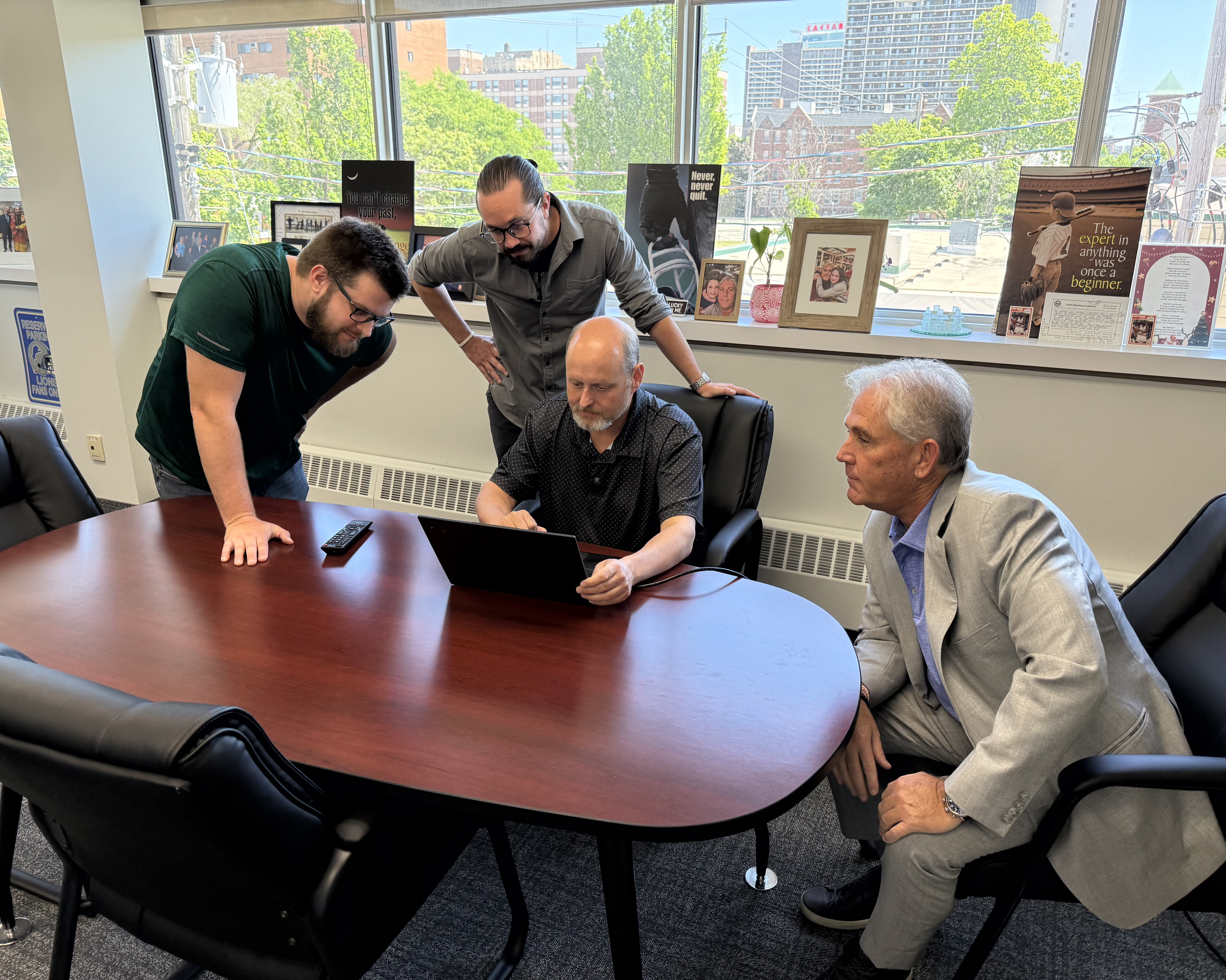 four men at a boardroom table looking at a computer